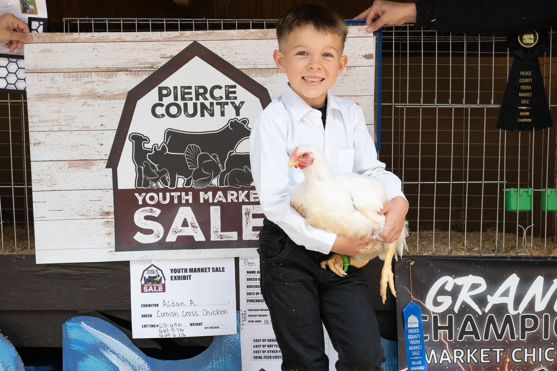 A smiling young exhibitor holds a white chicken in front of a PCYMS sign.